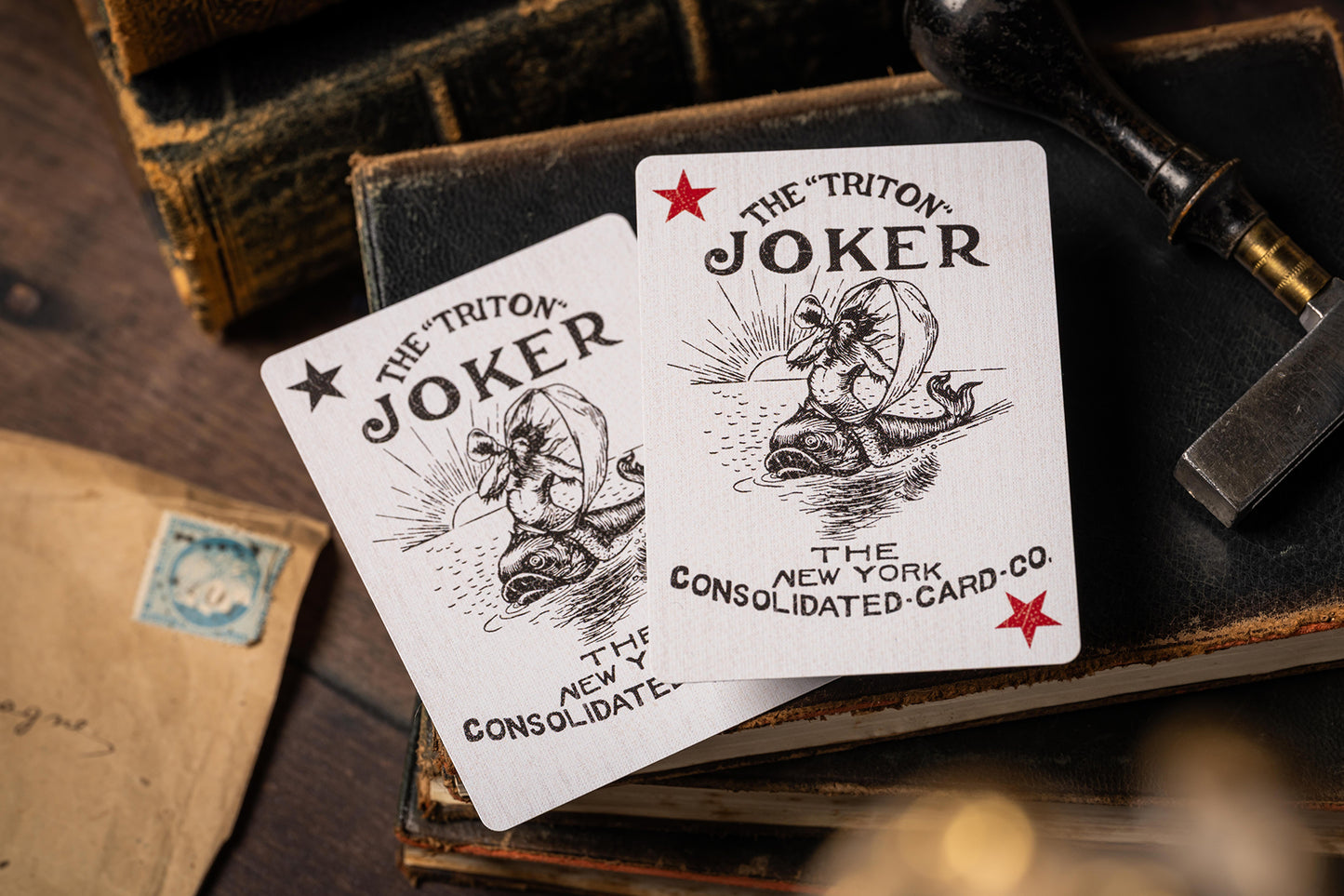 Two playing cards labeled 'The Triton Joker' on a wooden surface with vintage items.