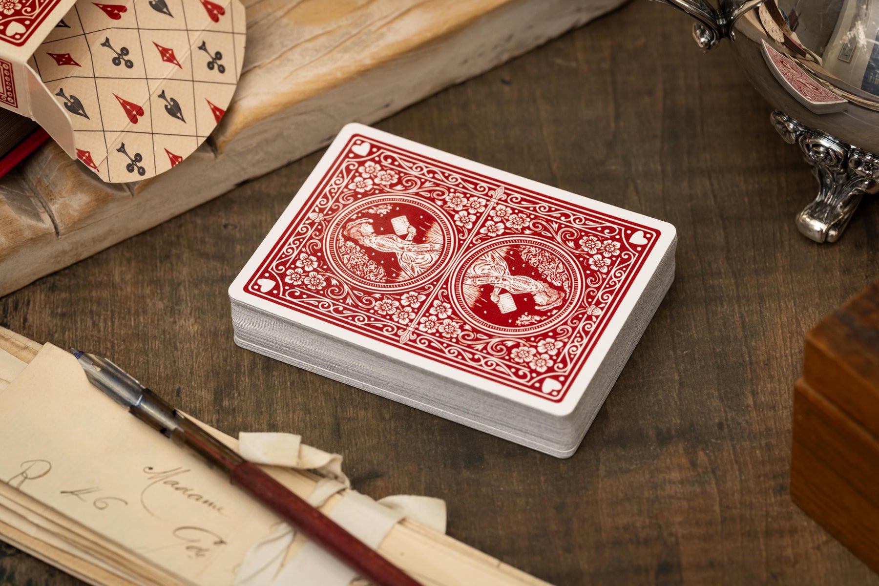 Stack of Love & Retribution playing cards with red and white design on a wooden surface with vintage items.