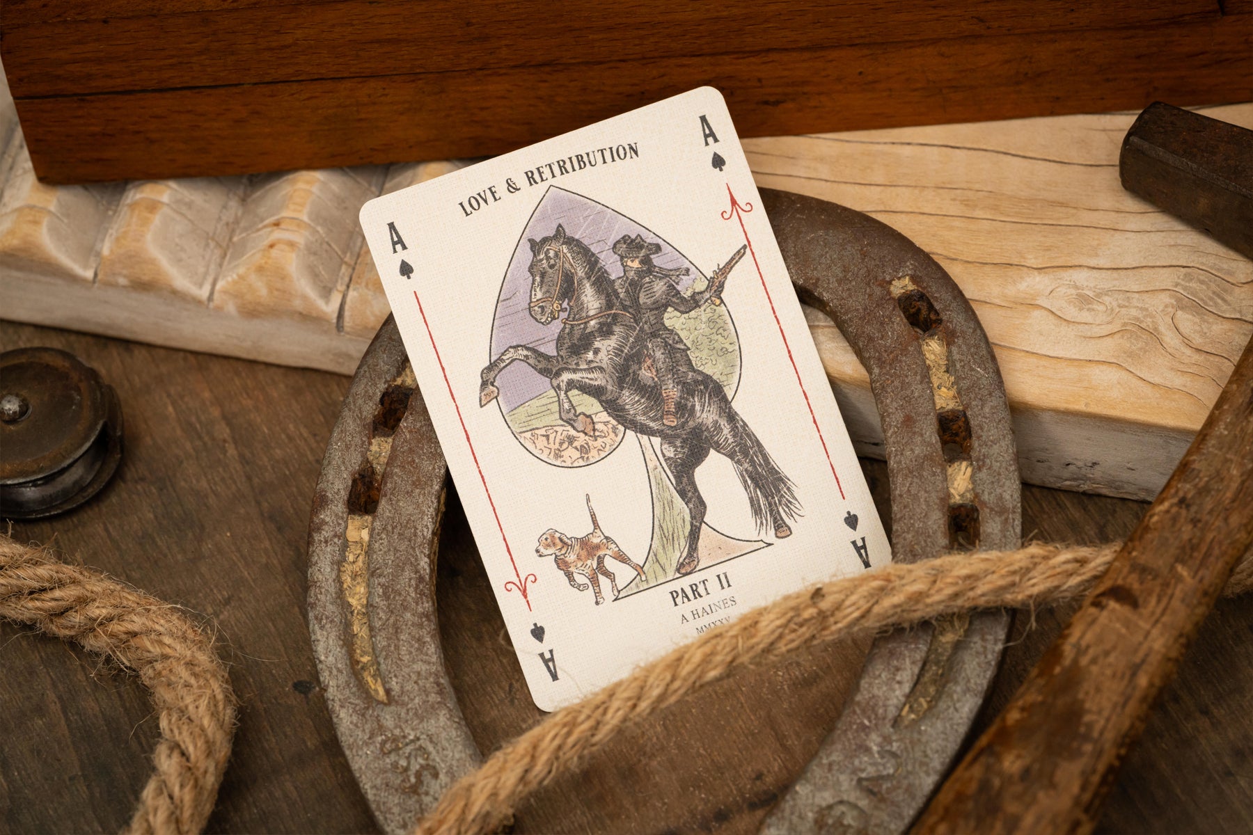 Playing card titled 'Love & Retribution' on a rustic wooden surface with a horseshoe.