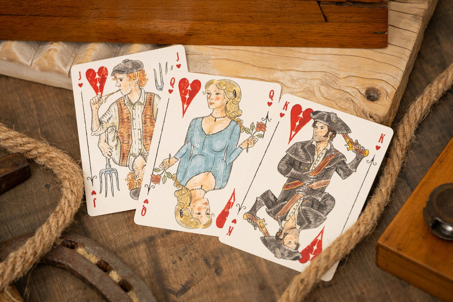 Three vintage playing cards featuring characters on a wooden surface with rope.