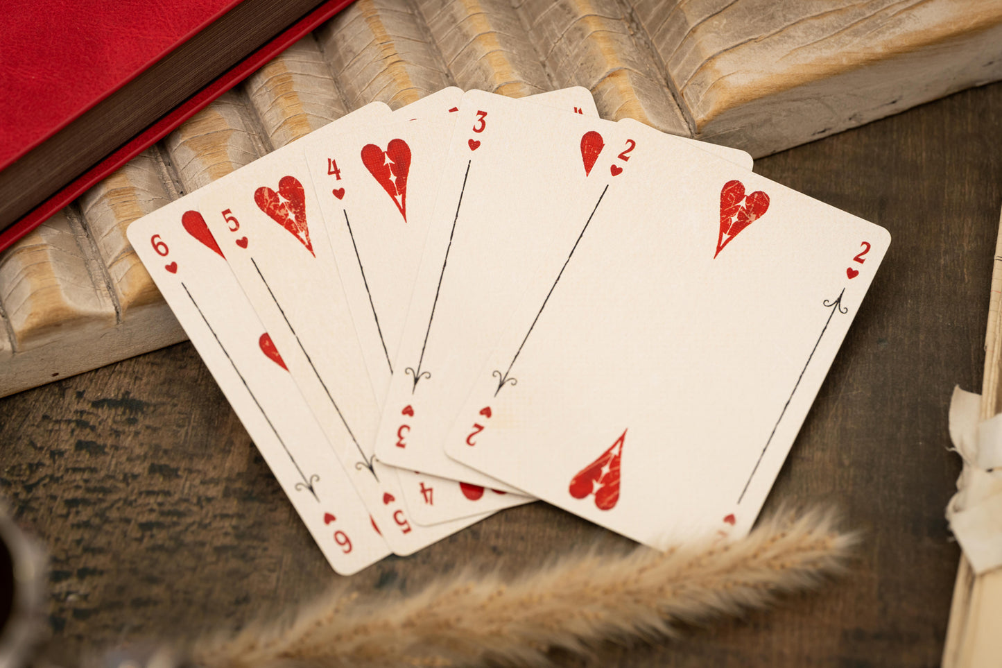 Five playing cards with red hearts on a wooden surface