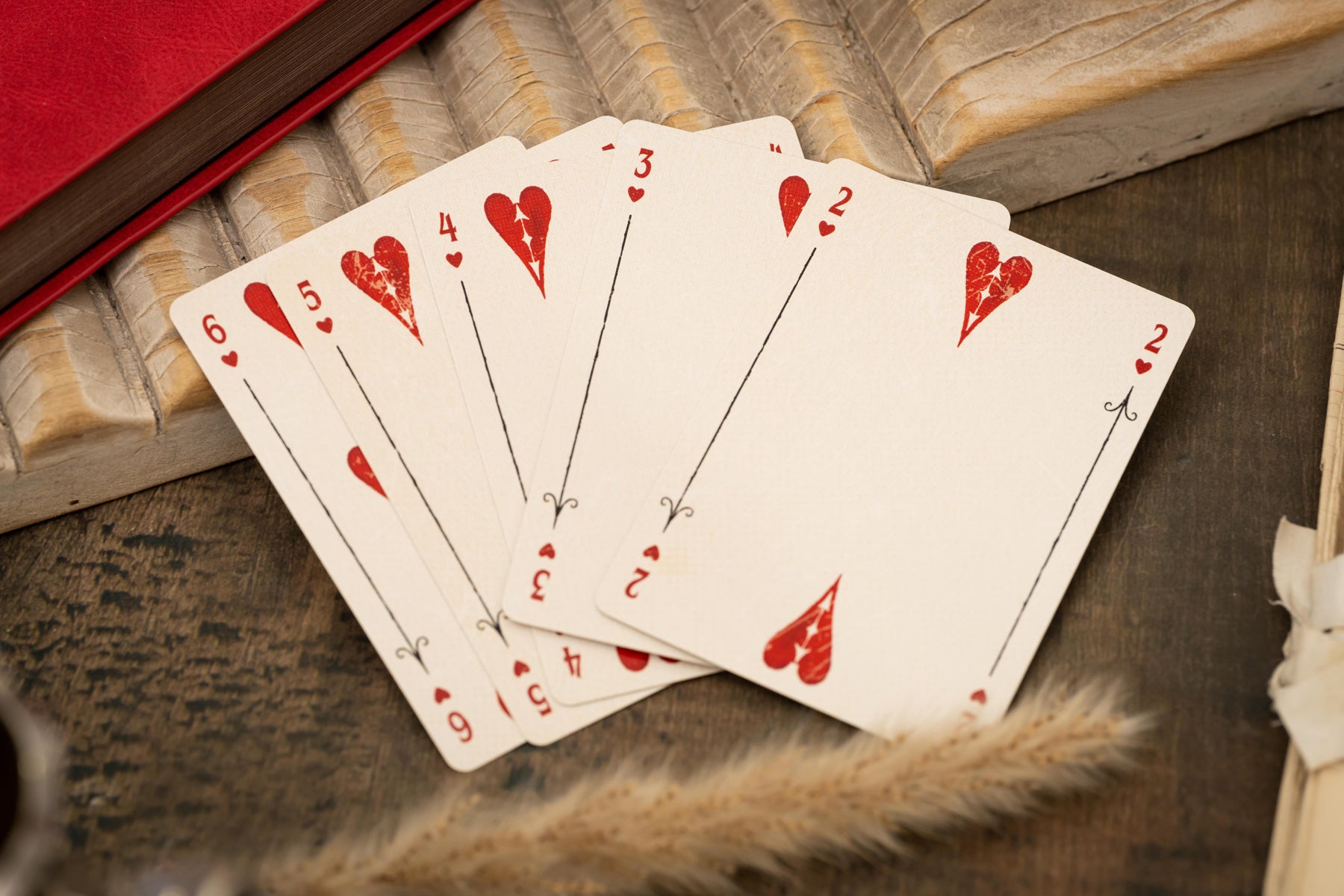 Five playing cards with red hearts on a wooden surface