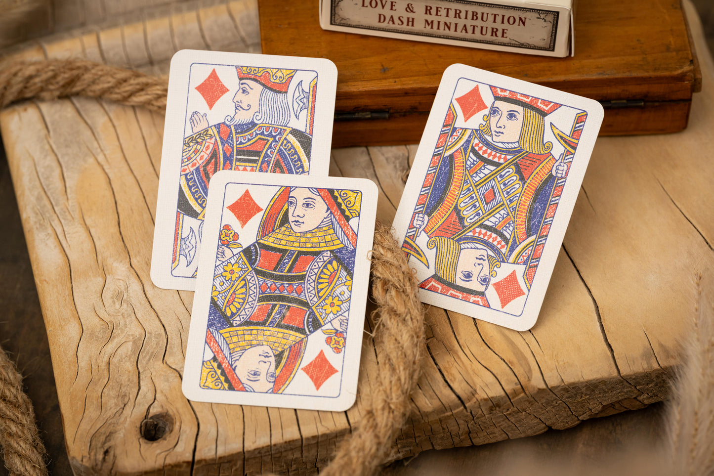 Three playing cards featuring queens on a wooden surface with a small wooden box in the background.