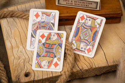 Three playing cards featuring queens on a wooden surface with a small wooden box in the background.