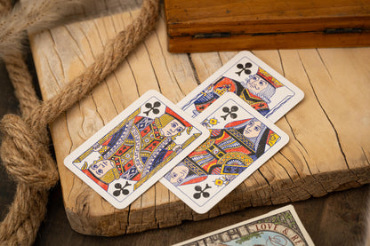 Three playing cards featuring queens on a wooden surface with rope.