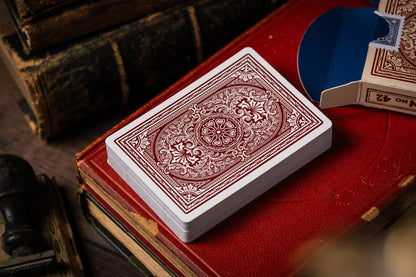 Red and white vintage playing card deck on a red surface with vintage books and cards in the background