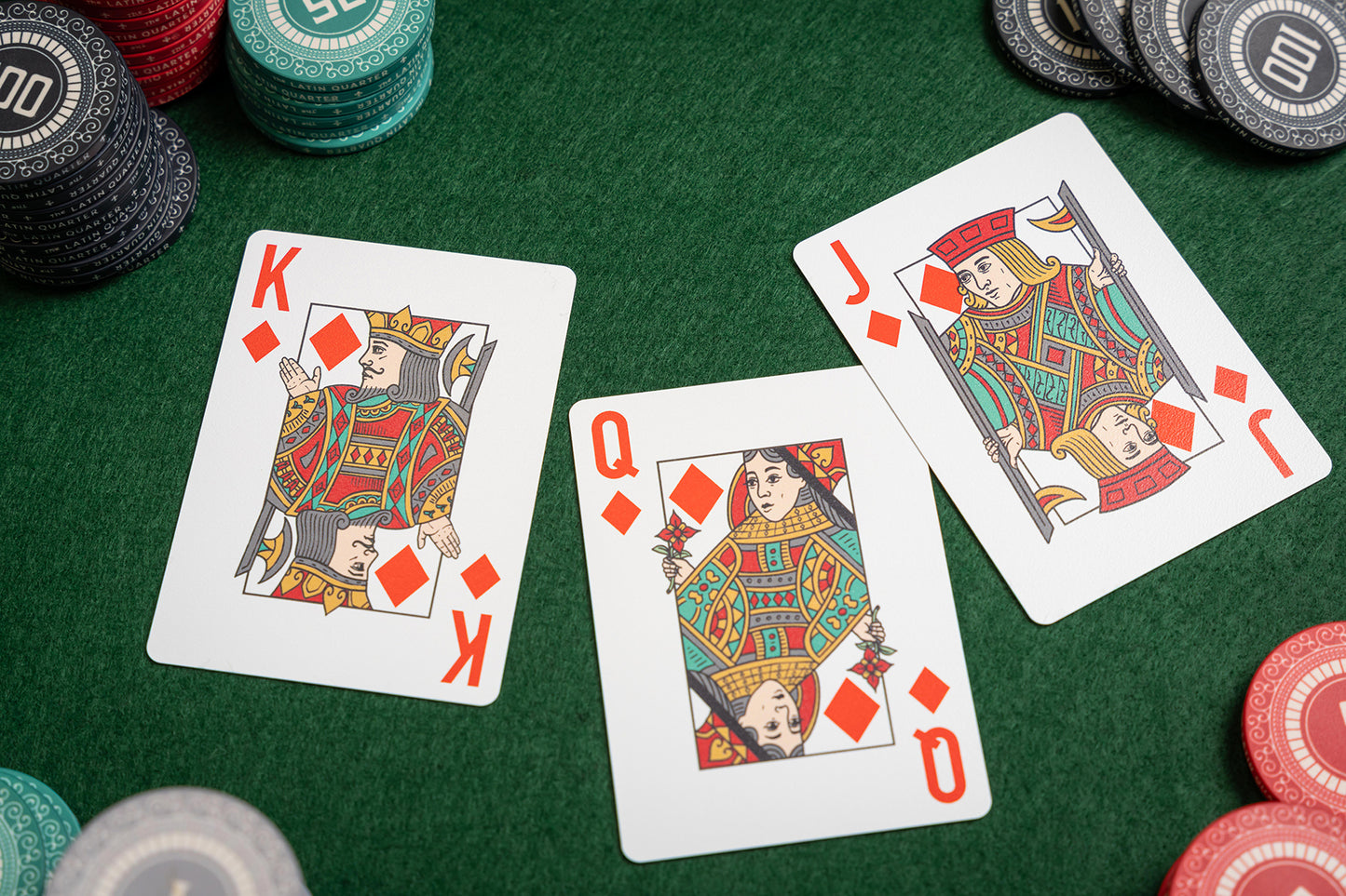 premium plastic Playing cards including King of Diamonds and Queen of Hearts on a green felt table with poker chips.