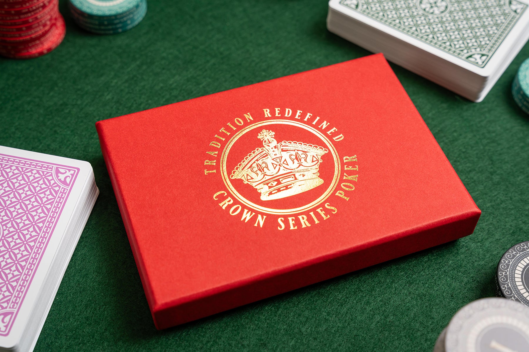 luxury Red playing card box with 'Crown Series Poker' gold foil logo on a green felt surface with playing cards and casino chips.