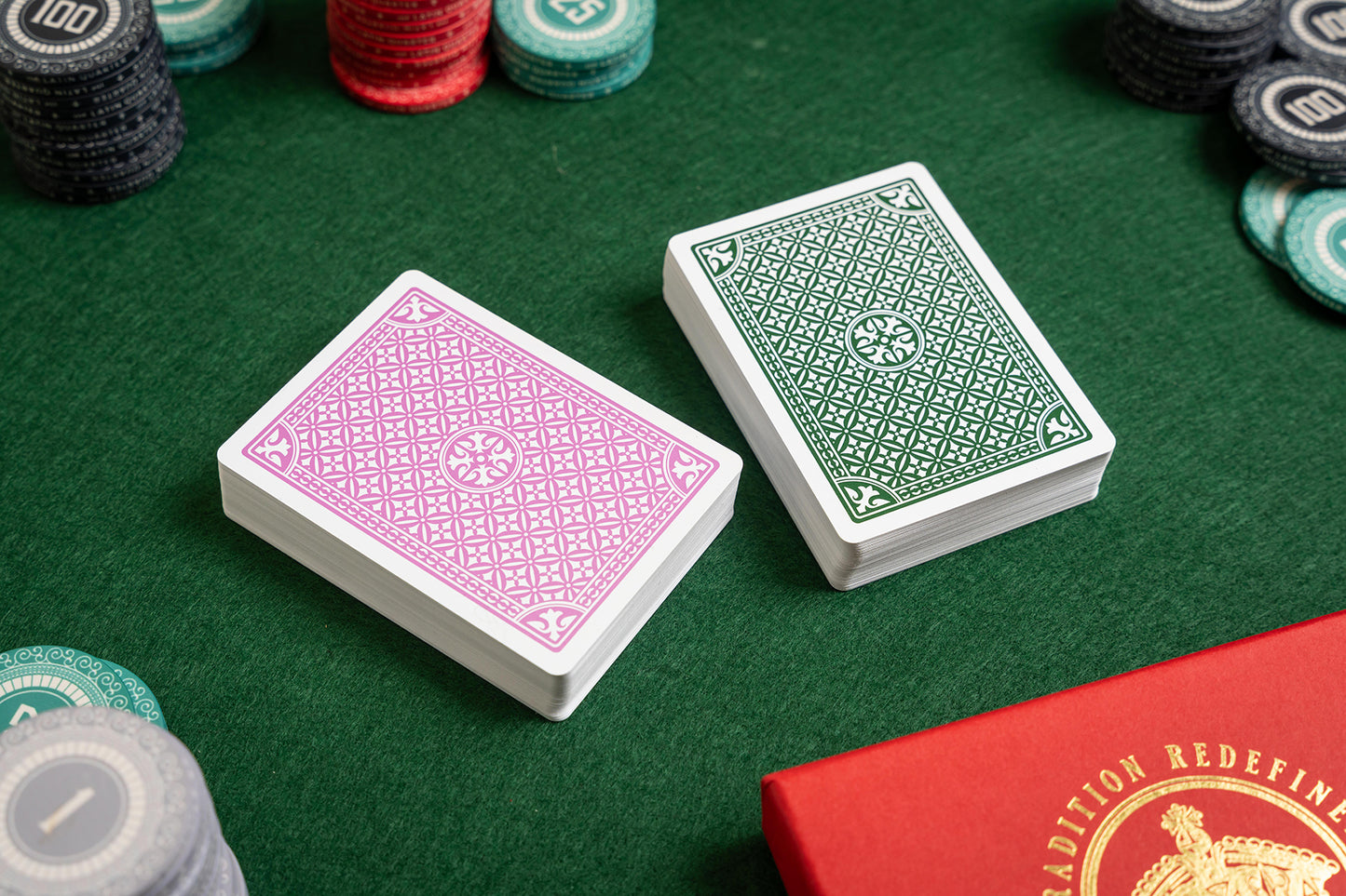 Two decks of pink and green premium pvc playing cards on a green felt surface with poker chips.