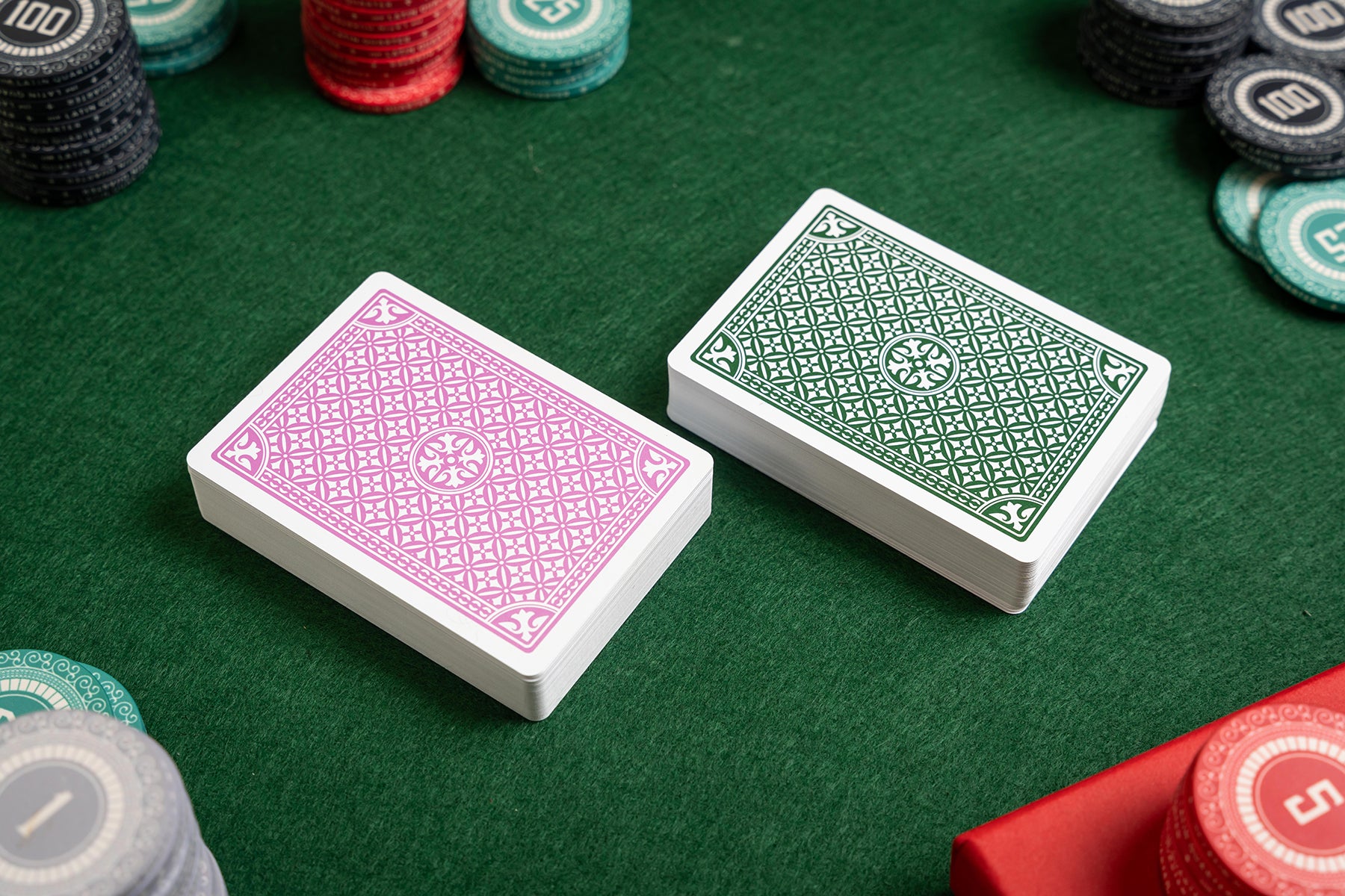 Two playing card decks on a green felt surface with poker chips around - premium plastic casino poker playing cards