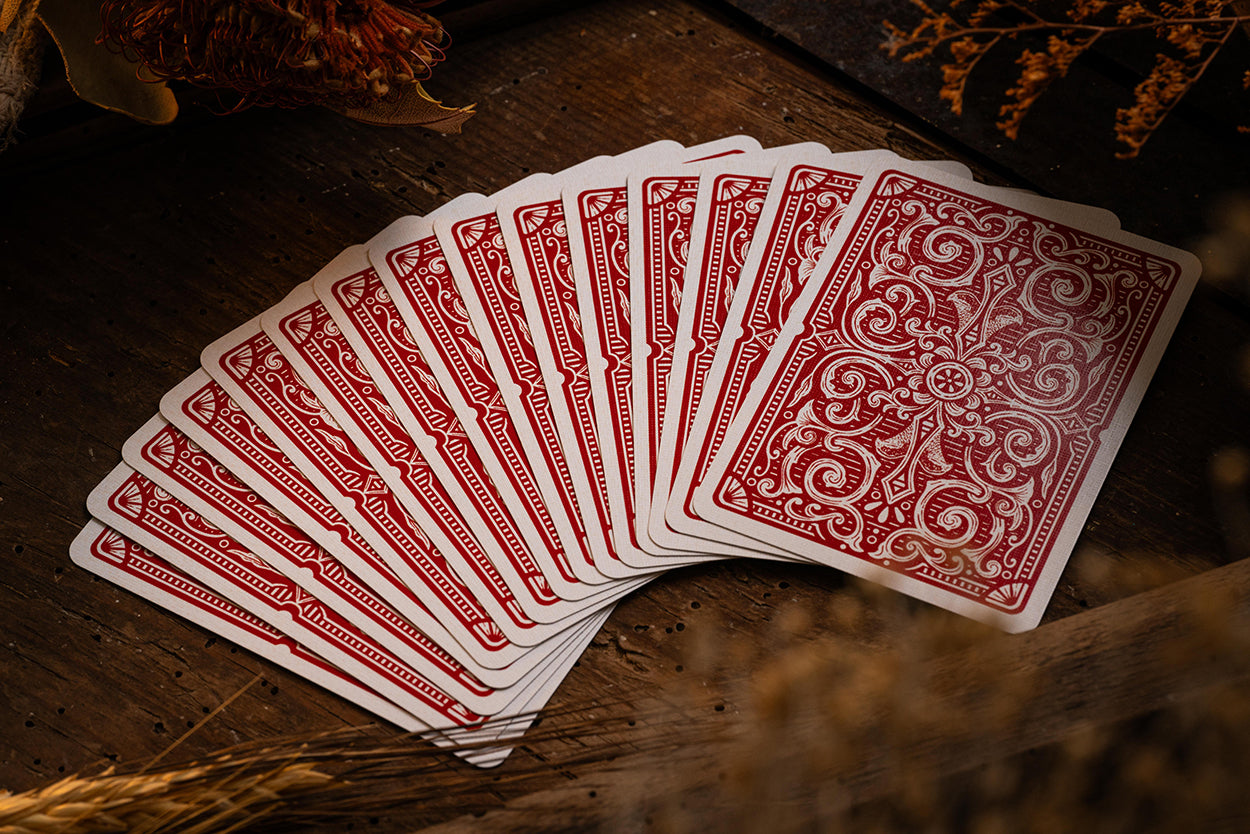 Fanned-out deck of red playing cards on a wooden surface with dried flowers.